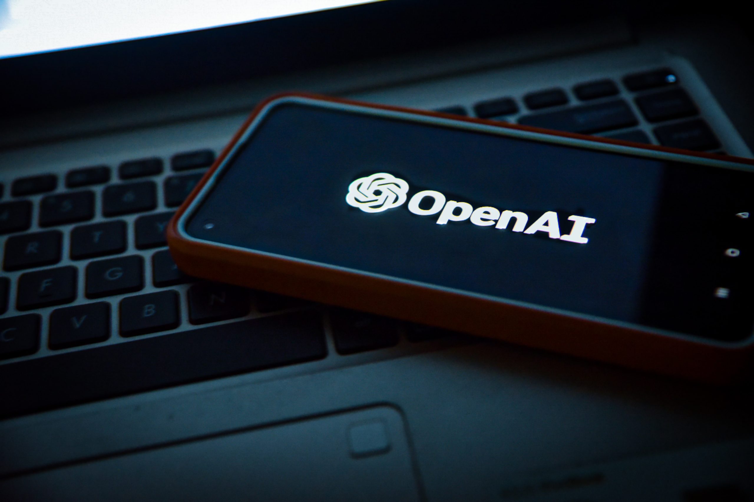 a phone with the OpenAI logo on the screen resting on a laptop keyboard