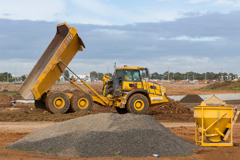 An orange coloured dump truck at a construction work site unloading dirt