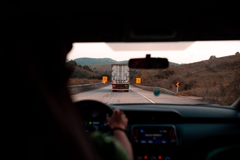 interior view of person with hands on steering while driving on a road behind a logistics fleet truck in Canada